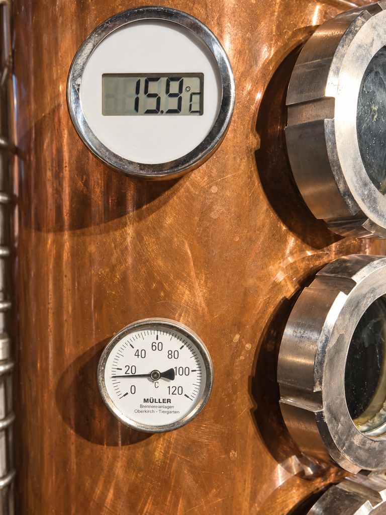 Nahaufnahme der kupfernen Brennsäule mit digitaler Temperaturanzeige bei 15,9 °C und analogem Thermometer.