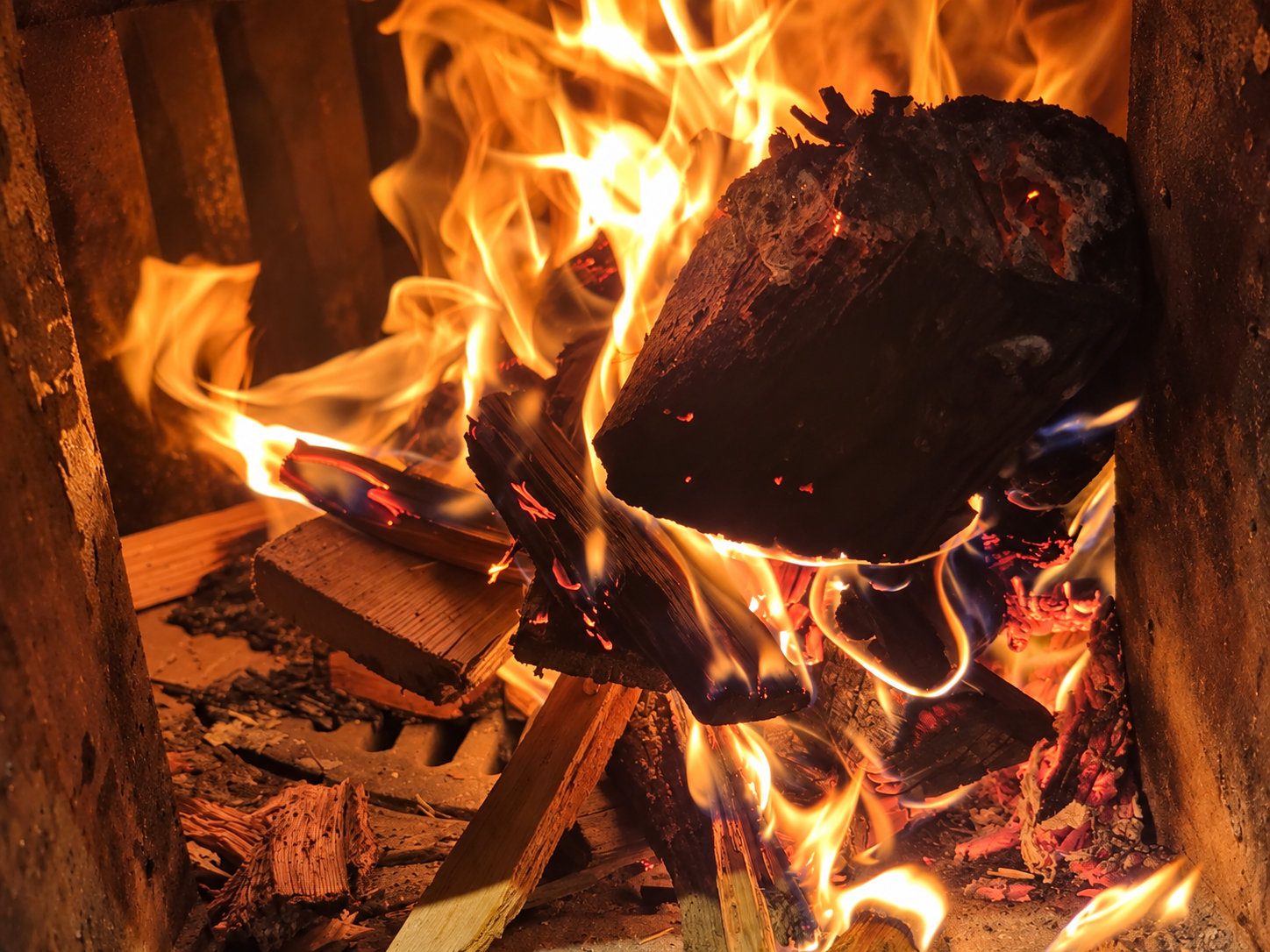 Brennende Holzscheite und orange leuchtende Flammen im Brennofen der Brennere